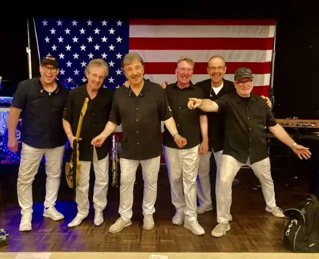 six members of the Embers featuring Craig Woolard standing in front of an American flag